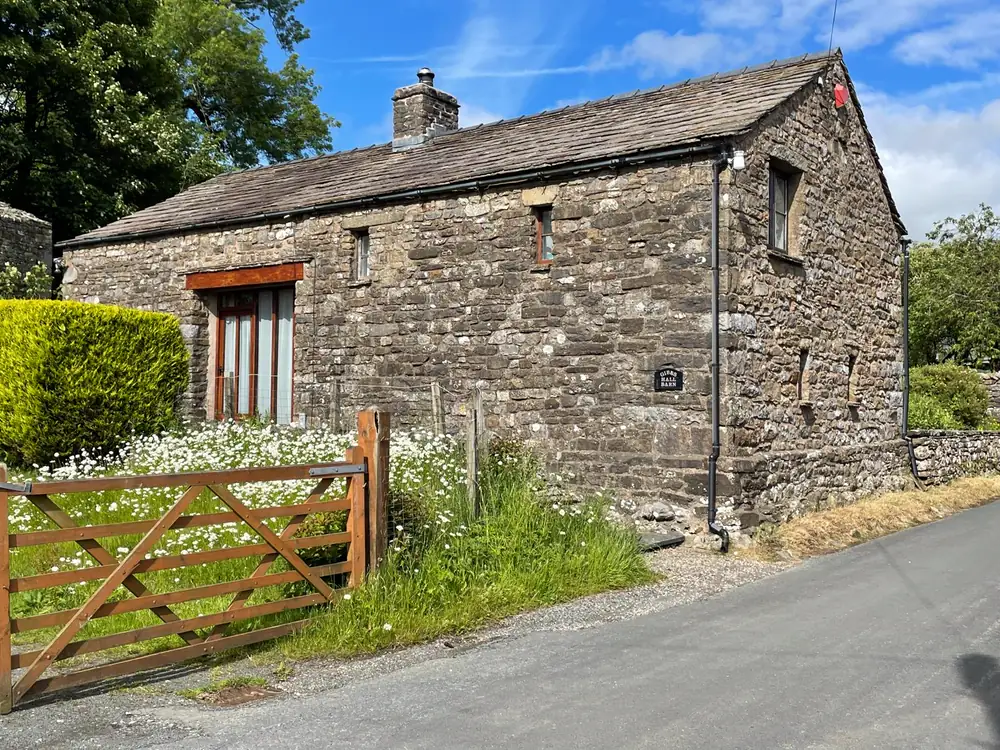 The stone exterior of Gibbs Hall Barn behind a wooden field gate
